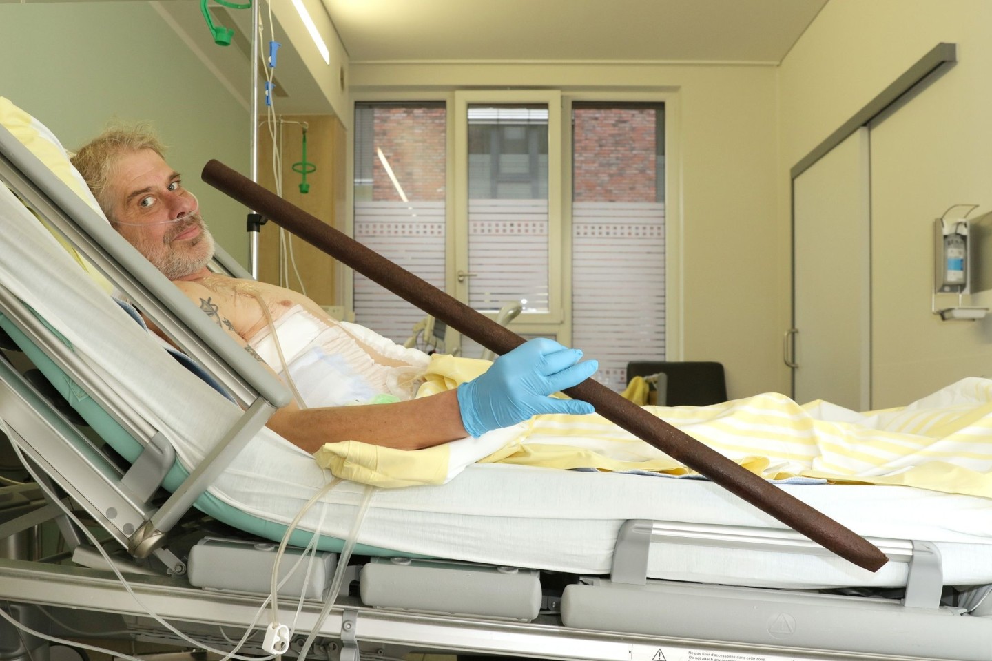 Patient Frank Vaorin liegt im Krankenhausbett und hält die Zaunstange in der Hand, die seinen Körper durchbohrte.