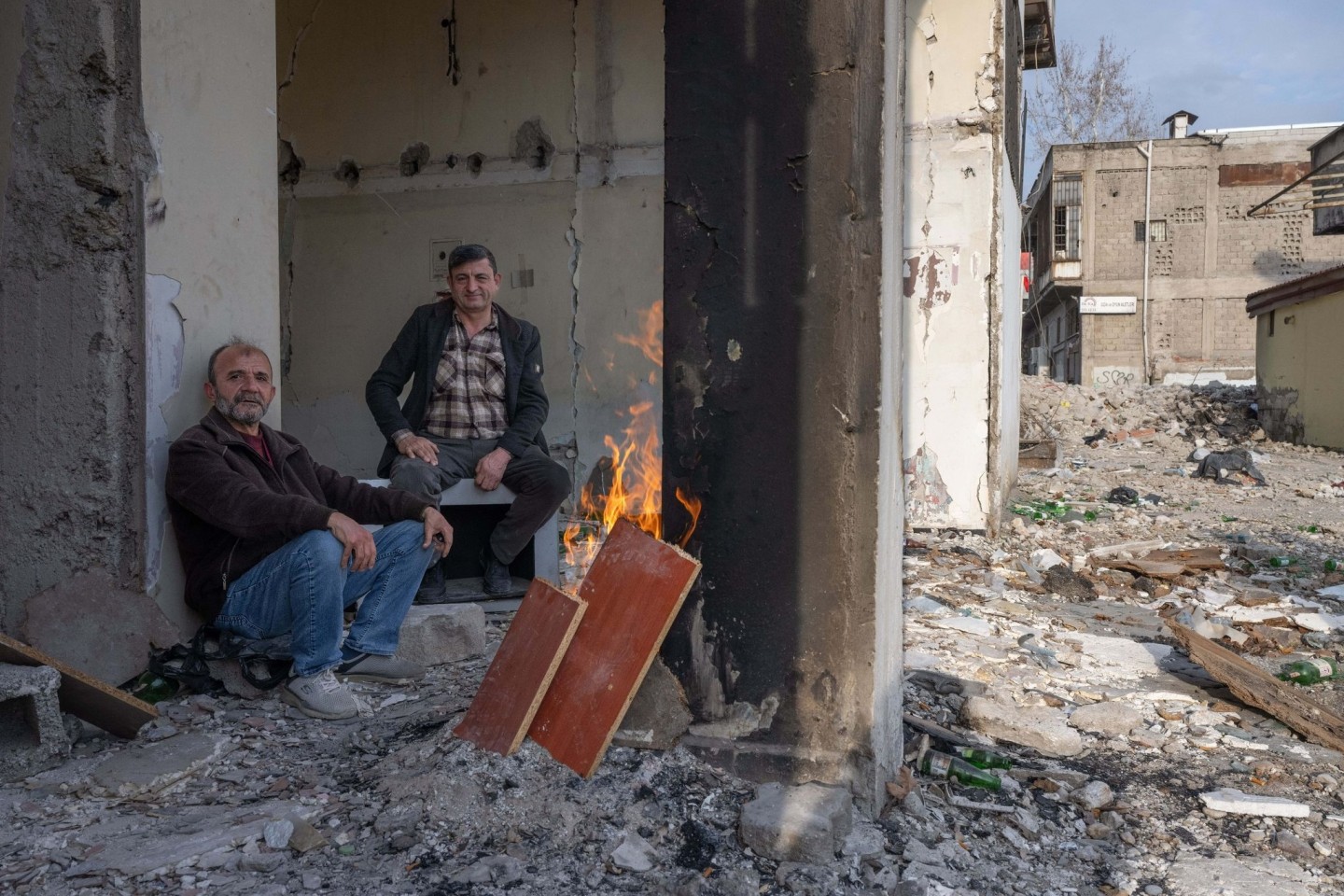 Zwei Männer wärmen sich in den Trümmern eines zerstörten Hauses in Kahramanmaras an einem Feuer. Im Zentrum der Stadt waren bei dem Beben vor einem Jahr unzählige Häuser zerstört oder...