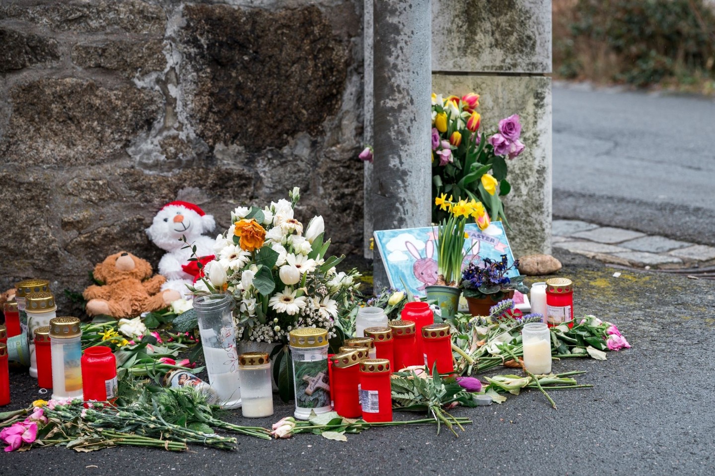 An einer Mauer vor dem Kinder- und Jugendhilfezentrum in Wunsiedel liegen Blumen, Kuscheltiere und Kerzen.